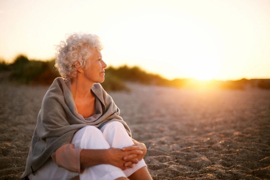 woman sitting alone on the beach looking out to the sunset