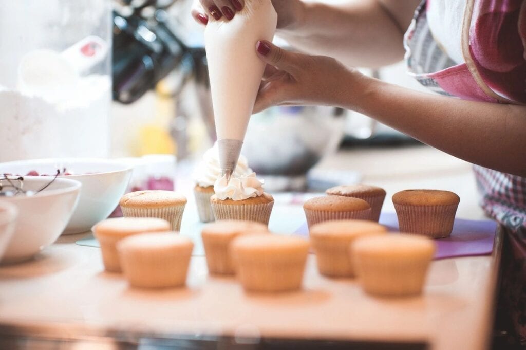 Photo of someone holding a pastry bag and putting white frosting on cupcakes